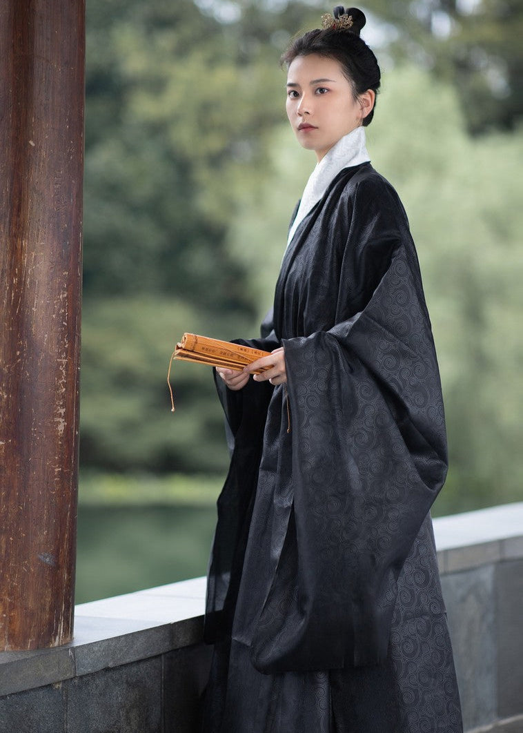 Person in traditional dark robe holding a wooden book against a blurred natural background