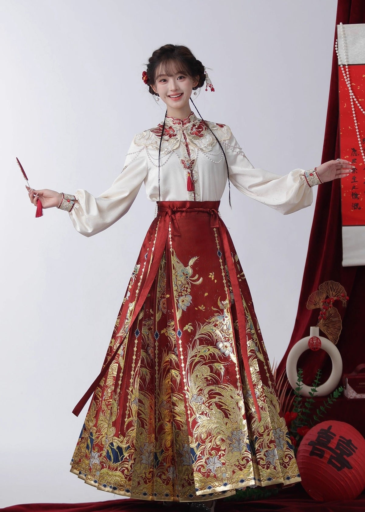 Traditional Chinese outfit with a white top and red skirt, holding a fan, on a plain background.